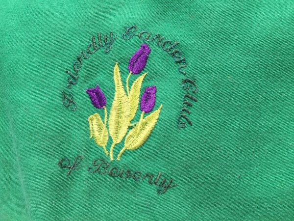 "Friendly Garden Club of Beverly" embroidered logo on a green apron.